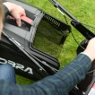 User securely reattaching the empty grass collection bag to the back of the Cobra MX484SPCE