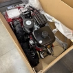 Top-down view into the opened shipping box, revealing the tightly packed, unassembled machinery and loose components inside.