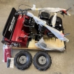 The fully unpacked machinery with the outer cardboard box removed, displaying the unassembled main unit on the wooden pallet and loose parts resting on the floor beside it.